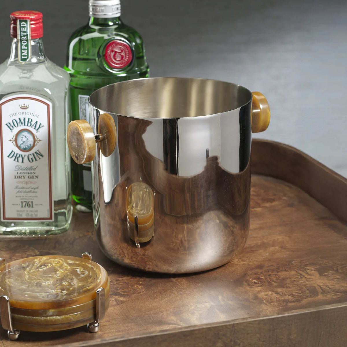 The ZODAX SPIGA ICE BUCKET - AMBER ACCENTS, featuring gleaming stainless steel with wooden side handles, adds a touch of style to your home decor.