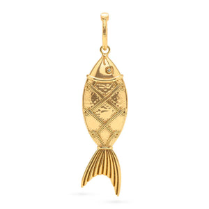 A person wearing the CAPUCINE DE WULF - POISSON PENDANT, featuring large interlocking rings of 18K gold over brass and a golden fish pendant, along with a matching gold ring. The person is wearing a blue top and their hand is touching the good luck talisman.