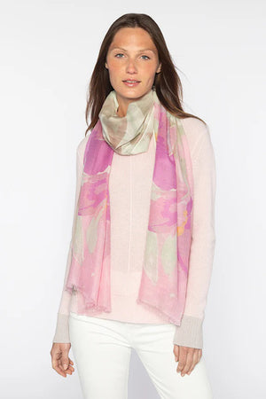 A person with long, dark hair stands against a plain background, elegantly wearing a KINROSS light blue cashmere sweater, white pants, and the KINROSS CASHMERE - KIWI BLOOMS PRINT SCARF.