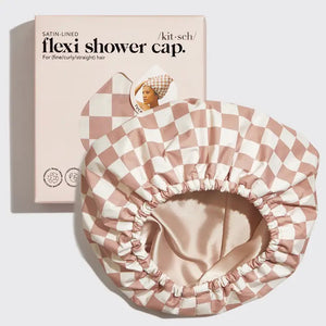 Displayed is the SATIN LINED FLEXI SHOWER CAP by KITSCH, featuring a white and brown checkerboard pattern. This cap boasts a waterproof shell and satin lining, suitable for fine, curly, or straight hair. The product packaging, which matches the cap's design, sits alongside it and showcases a photo of someone wearing the cap with an adjustable back wire closure.