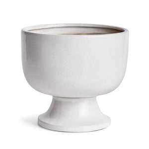 The ALBIE FOOTED CACHEPOT by NAPA HOME AND GARDEN is a white, ceramic, round planter with a simple, smooth design. It features a wide, shallow bowl on top that sits on a short, broad pedestal base. Finished with a shiny white glaze and slight crackled texture, it makes for a beautiful centerpiece while retaining its minimalist appeal.