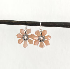 Two ANN LIGHTFOOT SEVEN POINT FACETED PINK MOONSTONE FLOWER EARRINGS hang from a dark rod, featuring faceted petals and a sterling silver weave, in a symmetrical design against a plain dark gray backdrop.