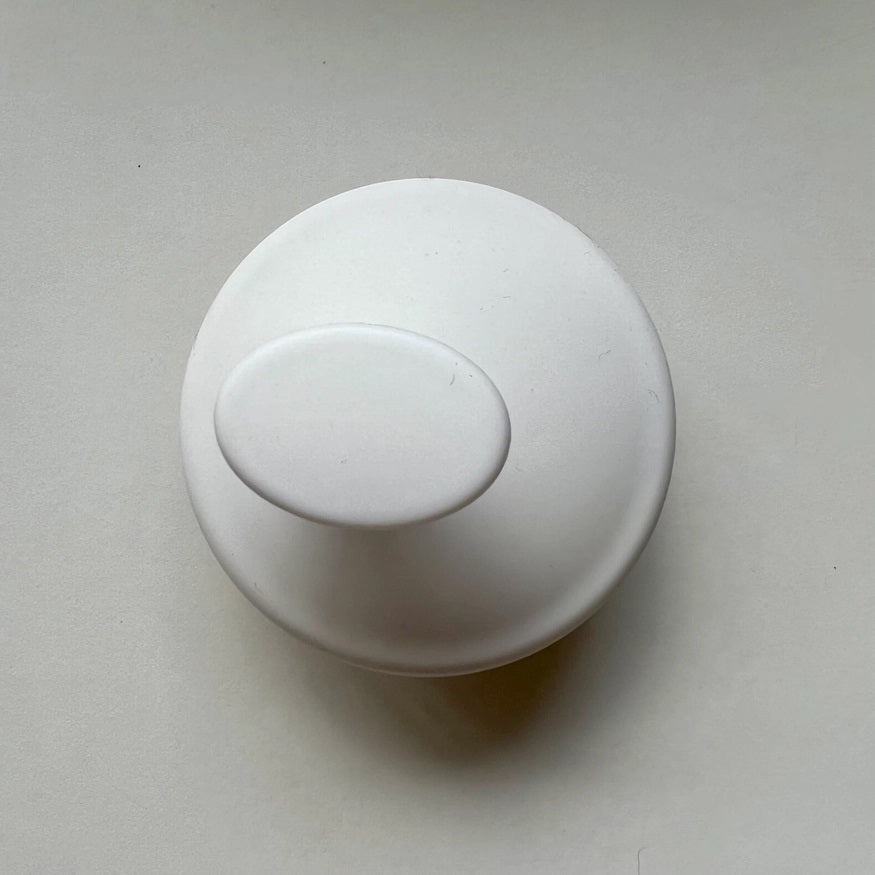 A white, round door knob with a smooth, oval-shaped handle is centered in the image against a plain, light-colored background. The unmarked handle appears clean and unadorned, reminiscent of the sleek design of the SCALP MASSAGING BRUSH by INDEX BY DEX.