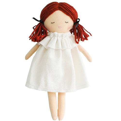 A child wearing a white long-sleeved shirt is seen holding the ALIMROSE - MINI MATILDA ASLEEP AWAKE doll, which has red hair and is snugly tucked into a floral-patterned sleeping bag. The cloth doll features a hood covering its head. The background displays a white textured surface, encouraging developmental play and social skills.