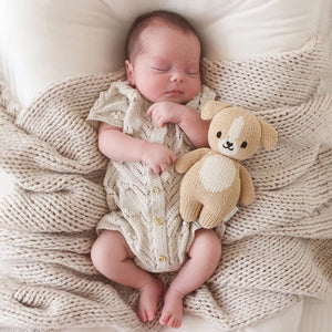 The CUDDLE + KIND - HANDMADE BABY PUPPY by CUDDLE & KIND is displayed from the back, highlighting its beige knitted body, small floppy ears, stubby arms, and short tail with no visible facial details. Meticulously hand-knit from 100% cotton yarn, its texture is distinctly visible, enhancing its cozy and handcrafted appeal. Perfect for those who appreciate fair trade and hand-knit baby animals.