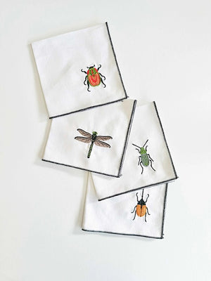 Four EMBROIDERED INSECT COASTERS from DOT AND ARMY are displayed in a 2x2 grid on a light surface. Each coaster, crafted in Georgia, features colorful embroidered insects: a red and black ladybug in the top left, an orange and black beetle in the top right, a green dragonfly in the bottom left, and a green bug in the bottom right.