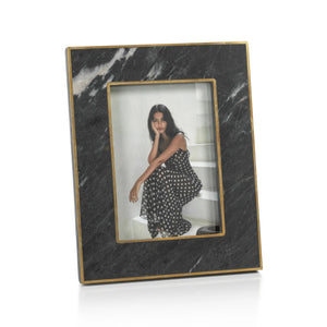 The ZODAX RENNES GRANITE PHOTO FRAME 5X7 features a rectangular black marble design with gold trim, showcasing a photo of a woman in a polka dot dress on white steps. This elegant frame adds sophistication to any space.