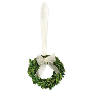 The BOXWOOD WREATH by NAPA HOME AND GARDEN features preserved English boxwood leaves in a compact green design. Adorned with a sheer white ribbon tied into a bow at the top and hung by a longer sheer white ribbon, this elegant piece of home decor is perfect for indoor use.