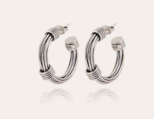 The GAS BIJOUX ARIANE SILVER HOOP EARRINGS are a stylish pair of silver hoops with a diameter of 2.7 cm, boasting a sleek and polished design accented by wrapped metallic threads at both the top and bottom. The reflective finish on the studs adds an elegant touch.