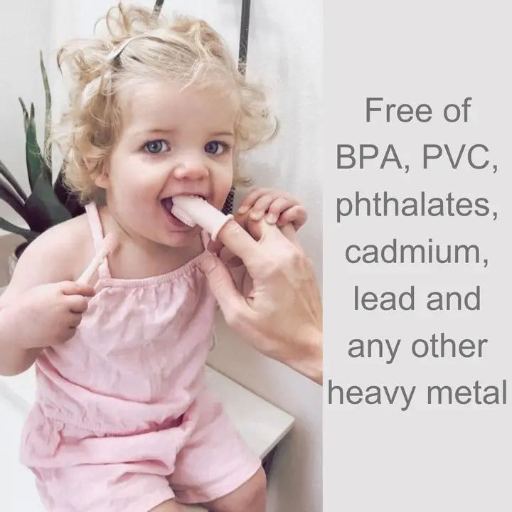 A child with curly blonde hair in a pink outfit is seated, holding a light-colored popsicle with the assistance of an adult&#39;s hand. Text on the right side of the image reads: &quot;Free of BPA, PVC, phthalates, cadmium, lead and any other heavy metal,&quot; highlighting the importance of safe materials for good oral hygiene using the SILICONE FINGER TOOTHBRUSH AND TONGUE CLEANER by ALI + OLI.