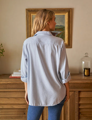 The Eileen Relaxed Button Up Shirt in Gray Blue by Frank & Eileen features a chest pocket, rolled-up sleeves, and bust-flattering button placement. Its inside label says "Frank & Eileen EST. 1947," and it is shown laid flat against a white background.