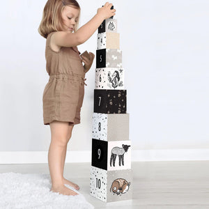 The WEE GALLERY - BABY ANIMAL NESTING BLOCKS, featuring monochrome animal illustrations and numbers, are perfect for developing early math concepts. The left stack includes woodland animals, while the right stack displays numbers 5, 6, and 7 adorned with more animal images. These nesting blocks from WEE GALLERY also help enhance motor skills against a plain white background.