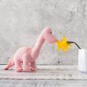 The DARK PINK KNITTED DIPLODOCUS TOY from BEST YEARS LTD stands against a white background. This soft, plush dinosaur features a long neck, small brown eyes, and short, stubby spikes along its back and tail. Its cozy texture makes it perfect for hugging—a delightful addition to newborn gifts.