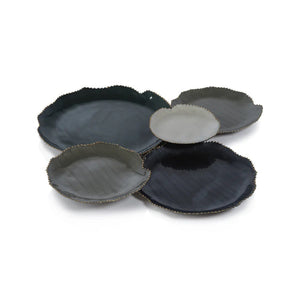 The ZODAX ENAMELED 5 CLUSTER SERVEWARE SET features five decorative plates arranged on a white surface. Each plate varies in size and displays shades of black and grey. The irregular edges are adorned with gold trim, giving the set an organic, leaf-like appearance.