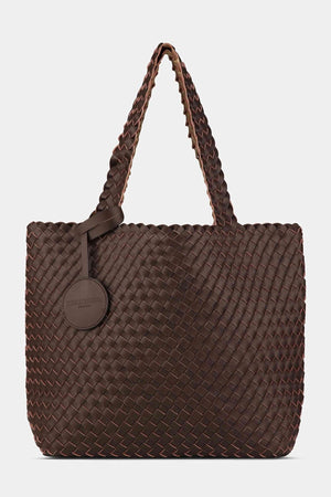 The WOVEN REVERSIBLE TOTE BAG by LINES OF DENMARK is a white tote featuring two shoulder straps and a circular faux-leather tag on one strap. This shopper showcases a textured, interlaced pattern and reversible design, providing stylish and elegant dual styling options. The image background is plain white.