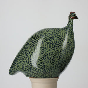 A LES CERAMIQUES DE LUSSAN ceramic sculpture, the LARGE CERAMIC FRENCH GUINEA IN GREEN SPOTTED COBALT, features a textured finish and stands on a small white pedestal against a plain backdrop.