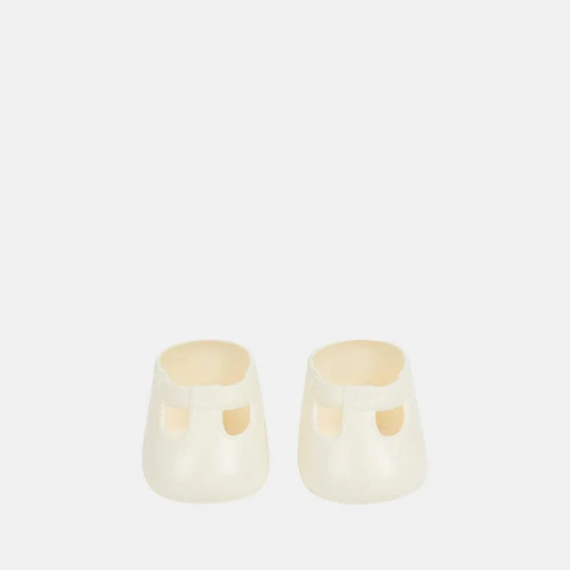 A close-up of a baby wearing OLLI ELLA USA DINKUM DOLL SHOES in Mallow Pink and white socks. The baby is seated on a soft, pale pink textured blanket, dressed in light brown clothing. Only the lower half of the baby&#39;s body is visible.