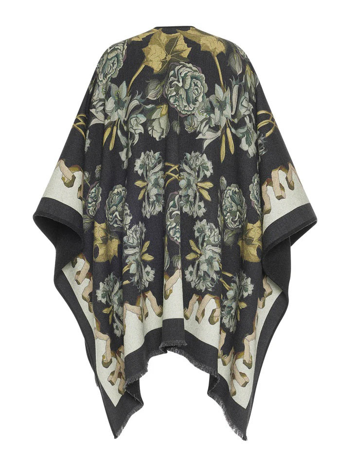 The "FRANCO FERRARI - ROSES AND DAFFODILS WOOL PONCHO" from the FRANCO FERRARI brand is a dark shawl adorned with a beige and green floral pattern featuring roses and daffodils. It has a fringed hemline and an asymmetrical shape for a draped, relaxed fit, giving it an elegant and nature-inspired appearance. This wool poncho is made in Italy.