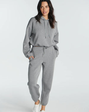 A person in SPANX - AirEssentials Jogger Pant in Heather Gray with a drawcord waist and matching sweatshirt stands with hands in pockets, paired with white sneakers. The luxuriously soft fabric against a plain white background highlights their cozy, relaxed style.