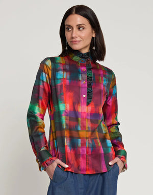 A person with shoulder-length dark hair is seen from behind, wearing the HINSON WU ATHENA LONG SLEEVE SATIN SHIRT in a festive plaid design that includes red, green, blue, and yellow shades. The outfit is complemented by blue pants and the shirt is machine washable for easy care.