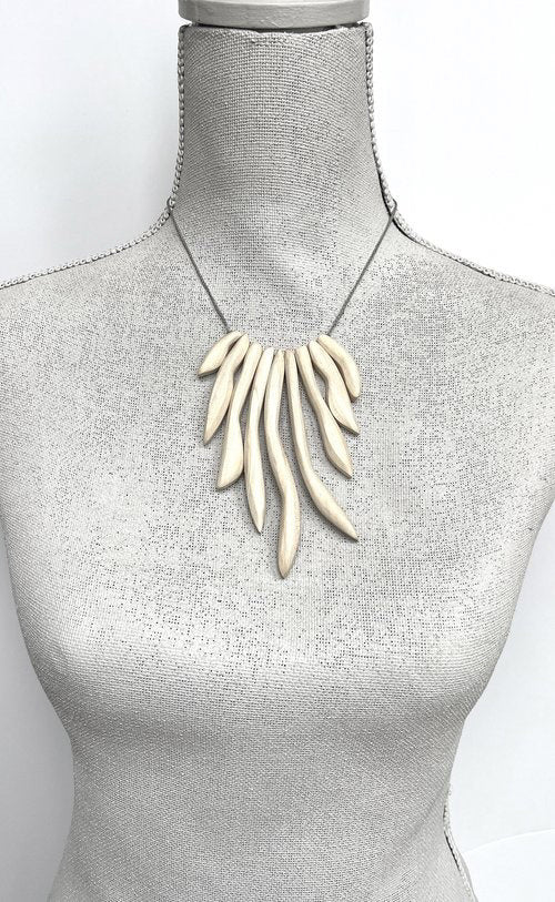 Introducing the ANN LIGHTFOOT - IRREGULAR WHITE WOOD FAN NECKLACE by ANN LIGHTFOOT, featuring a series of elongated, curved white wooden beads strung on a delicate grey cord. The hand-carved wood beads fan out symmetrically, resembling abstract spikes or pendants. Set against a plain white background.