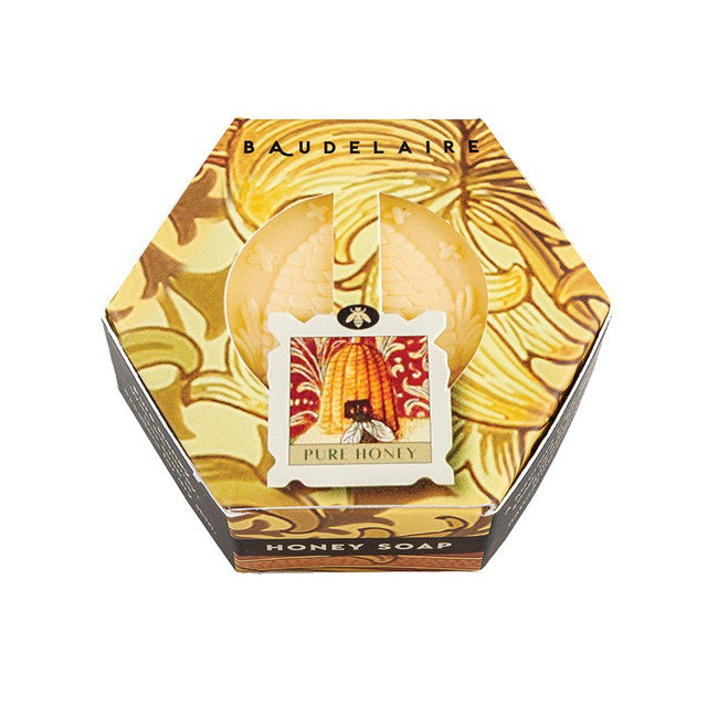 A hexagon-shaped box of BAUDELAIRE - PURE HONEY SOAP HEX BOX 3.5OZ, triple-milled for a luxurious lather with a decorative golden design featuring a skep beehive and flowers. The package has a small central label that reads &quot;Pure Honey&quot; and shows a honeycomb pattern and bee illustration, by the renowned brand BAUDELAIRE.