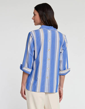 A woman with shoulder-length dark hair is wearing the HINSON WU - AILEEN IN BLUE AWNING STRIPE top, featuring blue and white stripes, button back detail, and 3/4 length sleeves. She pairs it with beige pants and stands against a plain white background, looking at the camera with a neutral expression.