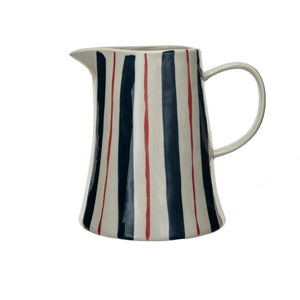 The 2 Quart Stoneware Pitcher with Stripes by Creative Coop features a flared base and a right-side handle. This white ceramic pitcher is adorned with hand-painted vertical stripes in navy blue, red, and white, creating an elegant pattern that covers its entire surface against a plain white background.