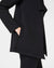 A person wearing the SPANX - AIRESSENTIALS DRAPE FRONT CARDIGAN in black, designed with long sleeves and crafted from lightweight fabric, elegantly poses with their hand in one of its pockets. The cardigan features an asymmetrical hem and is paired beautifully with black pants, highlighting the side and pocket details against a plain background.