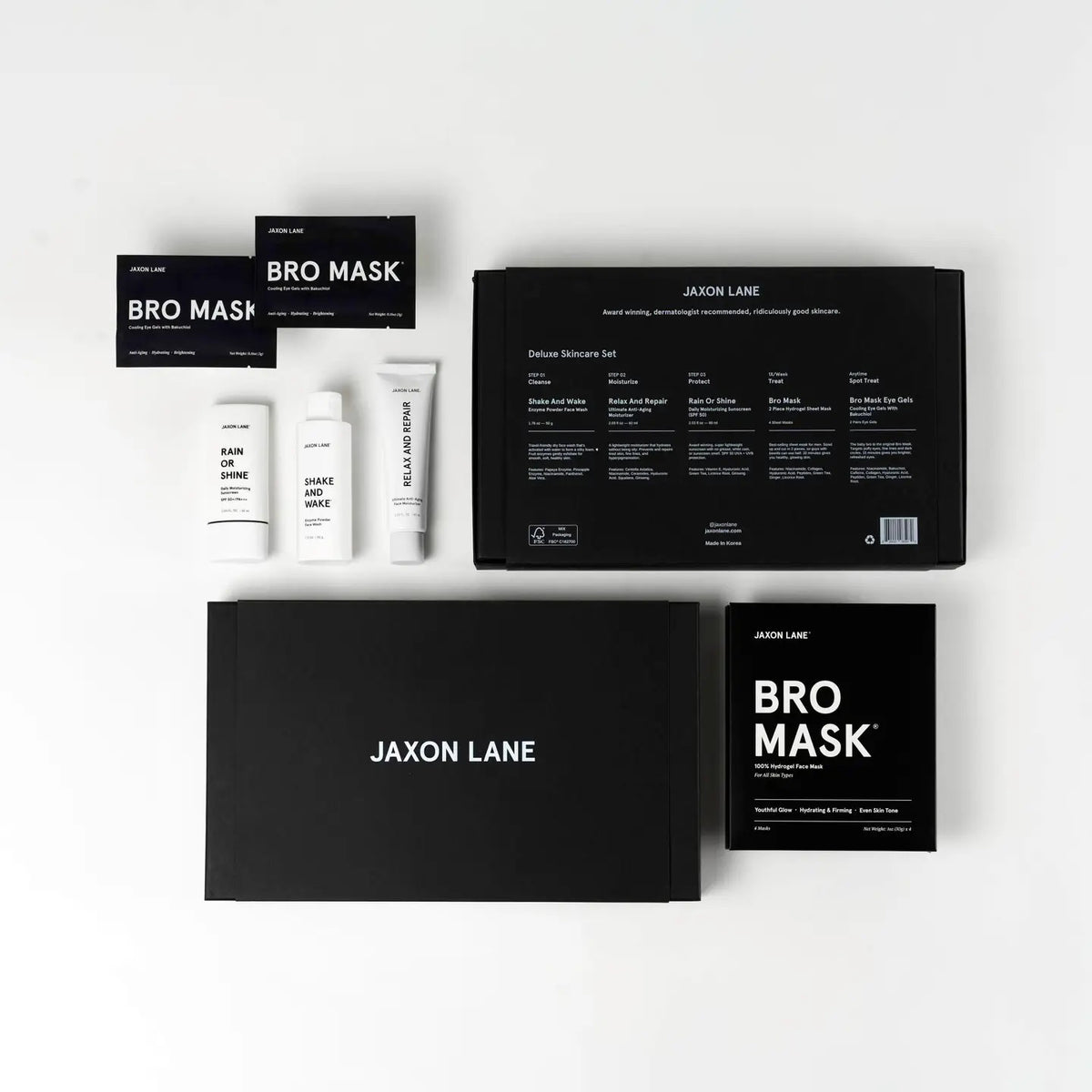 The JAXON LANE - DELUXE SKINCARE SET FOR MEN by JAXON LANE includes the BRO MASK, Rain or Shine sunscreen, Shake and Wake, and two large black boxes, all displayed neatly on a white surface.