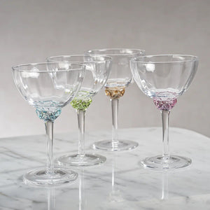 Product Description: The MARTINI COCKTAIL OPTIC GLASS set by ZODAX includes a rectangular wicker tray with metal handles, holding four stylishly crafted glass goblets, each featuring a vibrant decorative element on the stem. Ideal for serving drinks with flair, this elegant ensemble is showcased on a light gray surface.