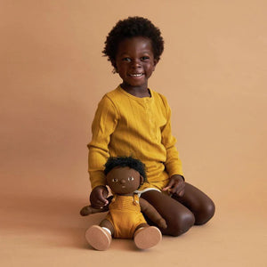 A DINKUM DOLL from OLLI ELLA USA features soft brown hair and comes dressed in a white knit romper paired with brown shoes. This charming doll has an embroidered face with brown eyes, a small nose, and a gentle smile. Its posable body makes it perfect for imaginative playtime, and it is posed standing upright.