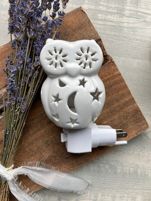 The OWL NIGHTLIGHT by LILY'S LIGHTS features a white ceramic owl design with cut-out star and moon patterns that allow light to shine through beautifully. Plugged into a white electrical base and set against a plain white background, this nightlight exemplifies quality craftsmanship, making it one of the most unique gifts.