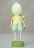 The ESC AND COMPANY - SHELDON FIGURINE, designed by Lori C. Mitchell and made by ESC AND COMPANY, INC, is a 6.25" tall poly resin piece with a round egg-shaped head, wearing a yellow shirt and striped green shorts on a green base, holding a white flower behind its back against a neutral background.