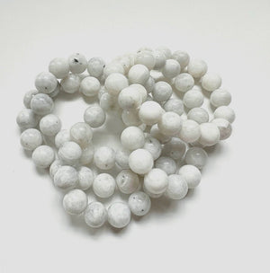 A string of round grey beads, possibly made of agate, arranged in a spiraled pattern against a plain white background, reminiscent of the elegant ANN LIGHTFOOT - GREY AGATE STRETCH BRACELET by ANN LIGHTFOOT.