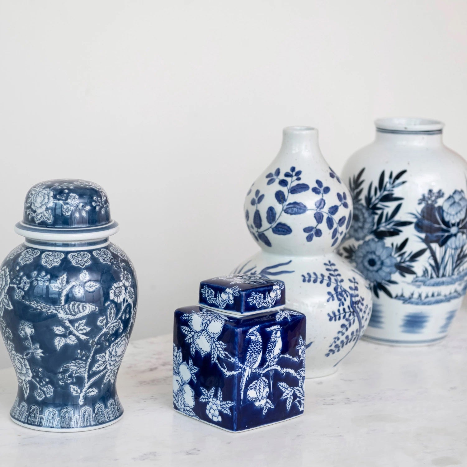 The HAND PAINTED CERAMIC GINGER JAR by CREATIVE COOP is a rectangular, dark blue and white ceramic piece adorned with white illustrations of two birds perched on a tree branch, surrounded by floral patterns. The jar includes a matching lid decorated with similar intricate designs.