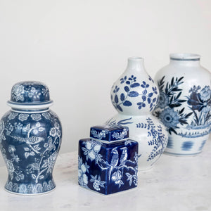 The HAND PAINTED CERAMIC GINGER JAR by CREATIVE COOP is a rectangular, dark blue and white ceramic piece adorned with white illustrations of two birds perched on a tree branch, surrounded by floral patterns. The jar includes a matching lid decorated with similar intricate designs.