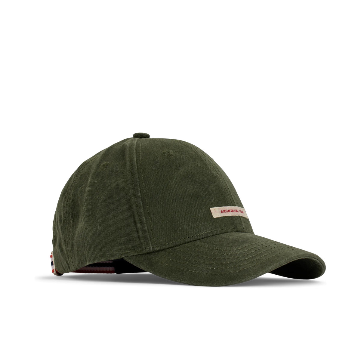 The AMUNDSEN SPORTS - WAXED COTTON CAP in navy blue is shown from the side against a plain white background, featuring a curved brim and an adjustable strap with a red, white, and black checkered norgesreima design.