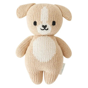 The CUDDLE + KIND - HANDMADE BABY PUPPY by CUDDLE & KIND is displayed from the back, highlighting its beige knitted body, small floppy ears, stubby arms, and short tail with no visible facial details. Meticulously hand-knit from 100% cotton yarn, its texture is distinctly visible, enhancing its cozy and handcrafted appeal. Perfect for those who appreciate fair trade and hand-knit baby animals.