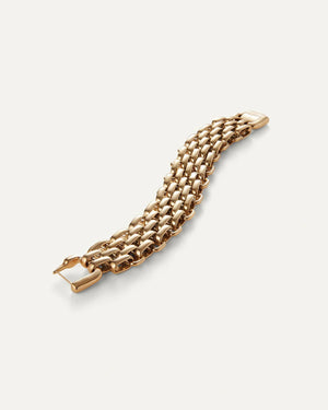 A person with long hair tied back in a sleeveless brown top gazes into the camera, resting their chin on their hand to highlight the JENNY BIRD PENELOPE LARGE BRACELET. The high-polish finish shines against the plain neutral background, keeping the focus on them.