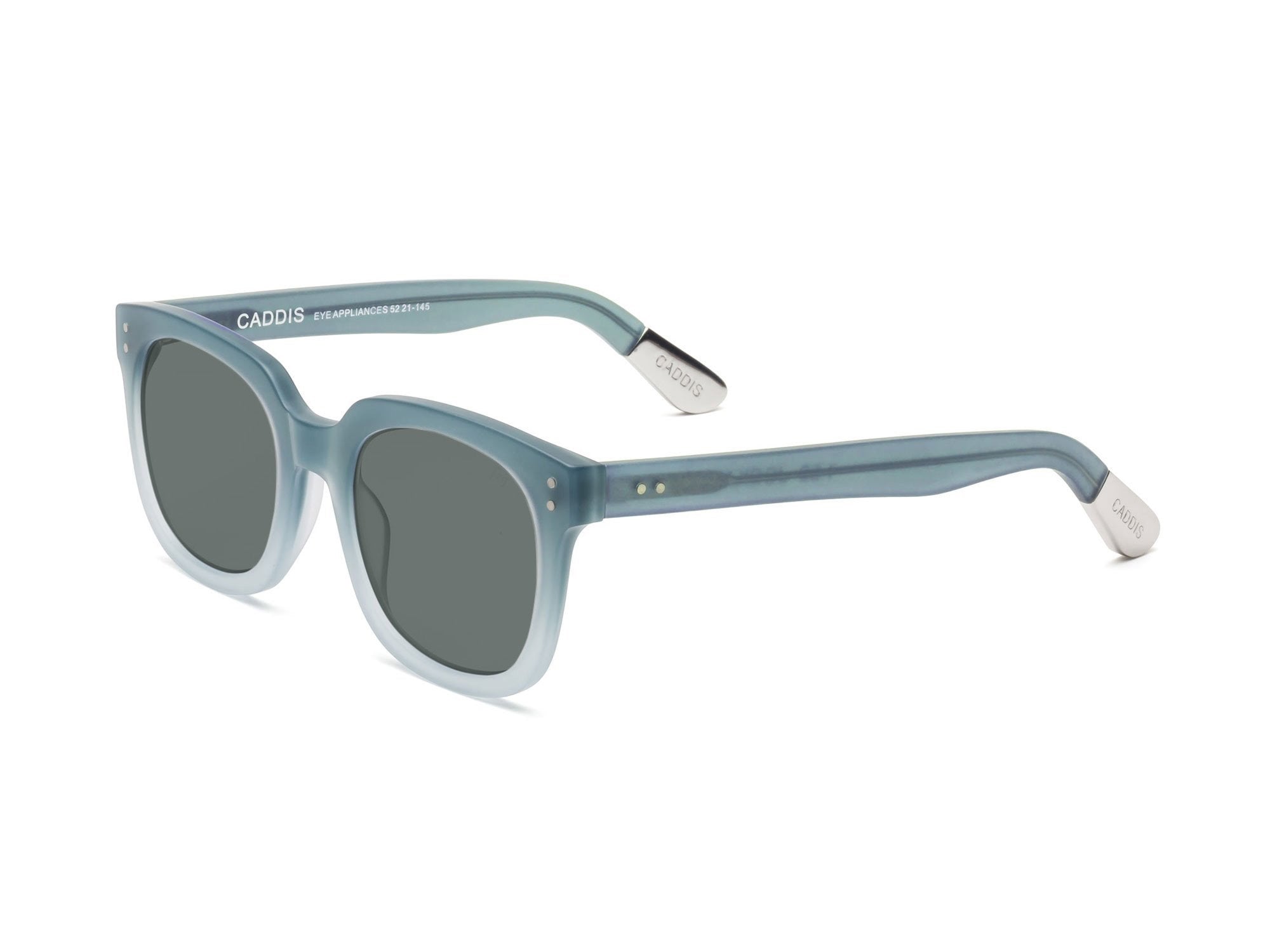 The CADDIS Jockamo Polarized Sunglasses feature a blue-green rectangular design with dark polarized lenses. The premium acetate frame is accented by white-tipped arms, and the brand "Caddis" is prominently displayed on both the lens and arm. These sunglasses combine a vintage aesthetic with a modern, sleek design perfect for casual wear.