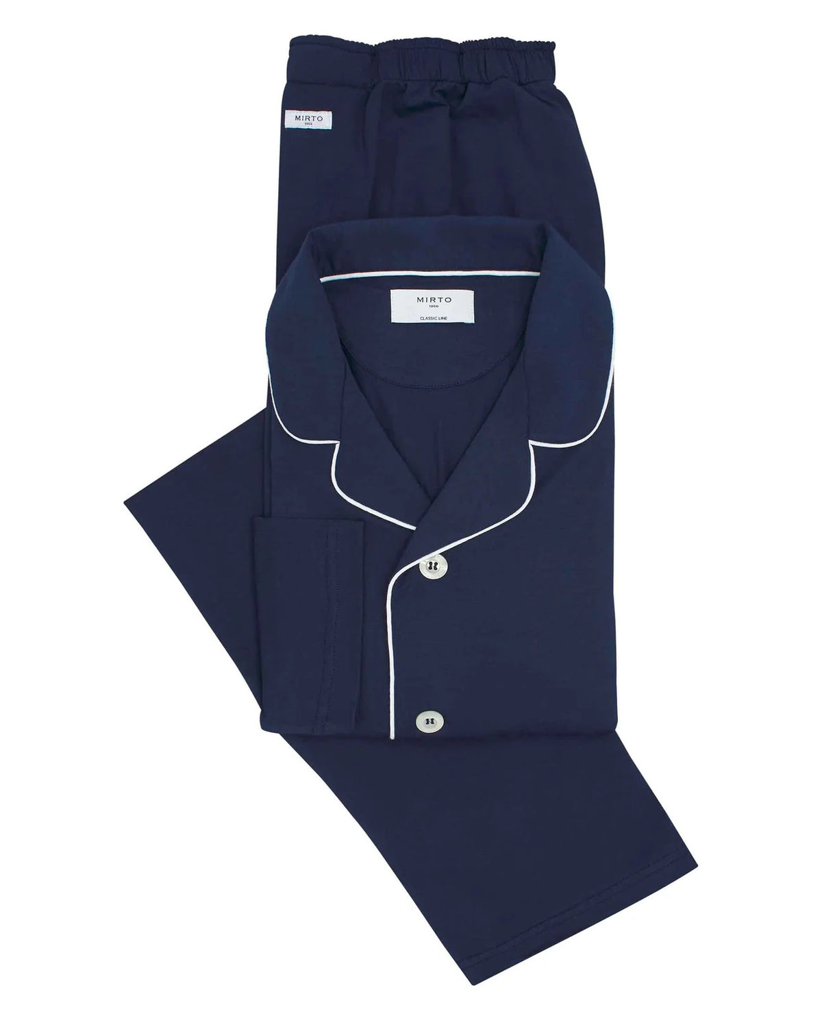 A person with short dark hair stands barefoot, facing sideways and looking back at the camera, wearing MIRTO 1956 Navy Modal Pajamas by MIRTO 1956 against a plain light background.