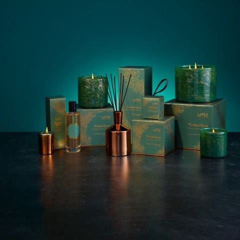 The LAFCO Woodland Spruce Holiday Candle, featuring a hand-blown glass vessel embellished with green and gold speckles, holds a soy wax candle against a plain white backdrop.