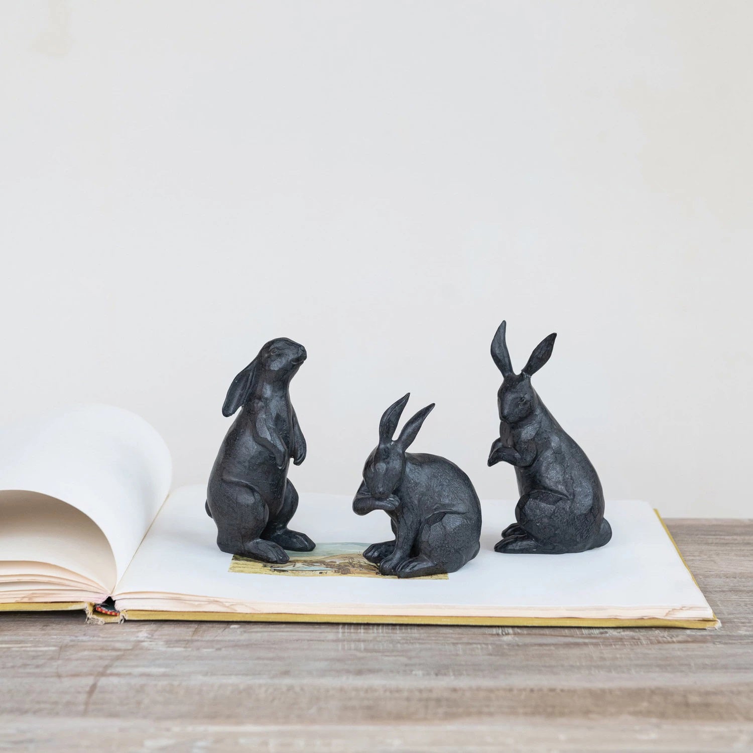 The CREATIVE COOP RESIN RABBIT WITH CAST IRON FINISH set features three dark sculptures: one sitting upright with alert ears, another standing tall on its hind legs, and the third grooming itself.