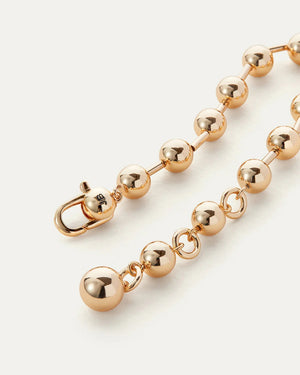 The JENNYBIRD Celeste Bracelet displays a series of gold beads with a high polish finish, connected by a fine chain, all set against a white background. A larger bead functions as the clasp for this elegant piece.