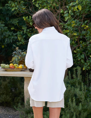 The FRANK AND EILEEN - EILEEN RELAXED BUTTON UP IN TRIPLE FLEECE WHITE features a collared neckline, buttons down the front, and a single chest pocket. The long sleeves are rolled up, and the inside collar label reads "Frank & Eileen EST 1947." With its relaxed fit and slightly curved hem, it exudes a casual, laid-back vibe.