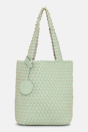 The WOVEN REVERSIBLE TOTE BAG by LINES OF DENMARK is a white tote featuring two shoulder straps and a circular faux-leather tag on one strap. This shopper showcases a textured, interlaced pattern and reversible design, providing stylish and elegant dual styling options. The image background is plain white.