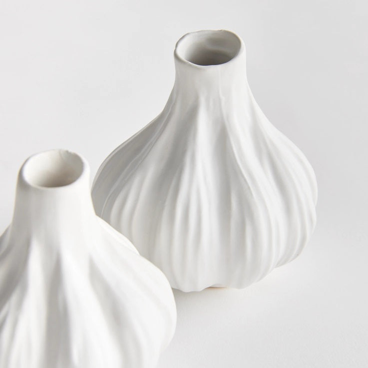 Two ALBURY BUD VASES from NAPA HOME AND GARDEN, each crafted from white ceramic and shaped like garlic bulbs, are placed side by side. One vase is slightly taller than the other, both featuring a smooth texture and flared bases. The plain white background emphasizes the elegant simplicity of their sculpted bodies.