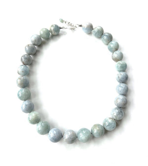 The ANN LIGHTFOOT - AQUAMARINE RAS DU COU NECKLACE is a breathtaking piece featuring large, round, polished beads in varying shades of light blue and green. The beads are intricately strung together and secured with a sterling silver clasp at the back. Arranged beautifully on a white background, this necklace offers an adjustable length for versatile wear.