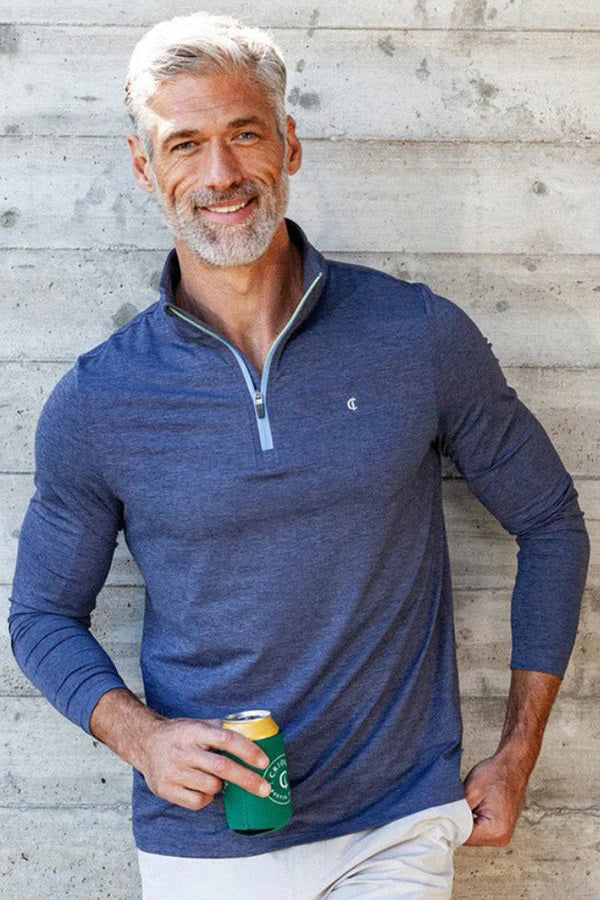 A man wears the CRIQUET FEATHER Performance Knit Quarter Zip Pullover in blue, featuring moisture-wicking fabric, a light blue zipper, and a small chest logo, standing against a plain white background.